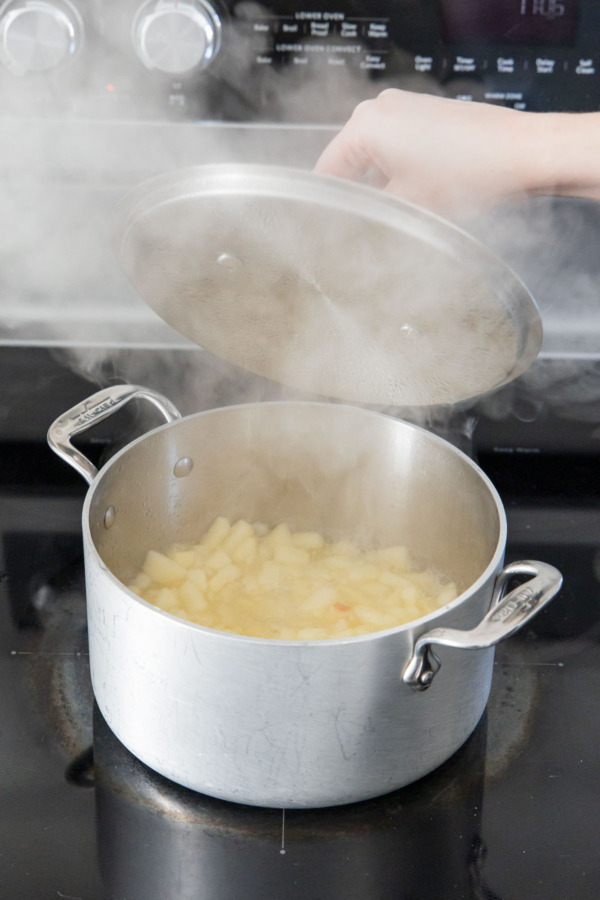 Uncovering the saucepan full of steaming soft apples on the stovetop.