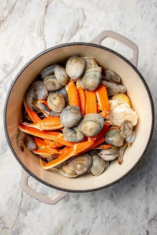 Overhead view of clams, shrimp, and crab legs added to Dutch oven