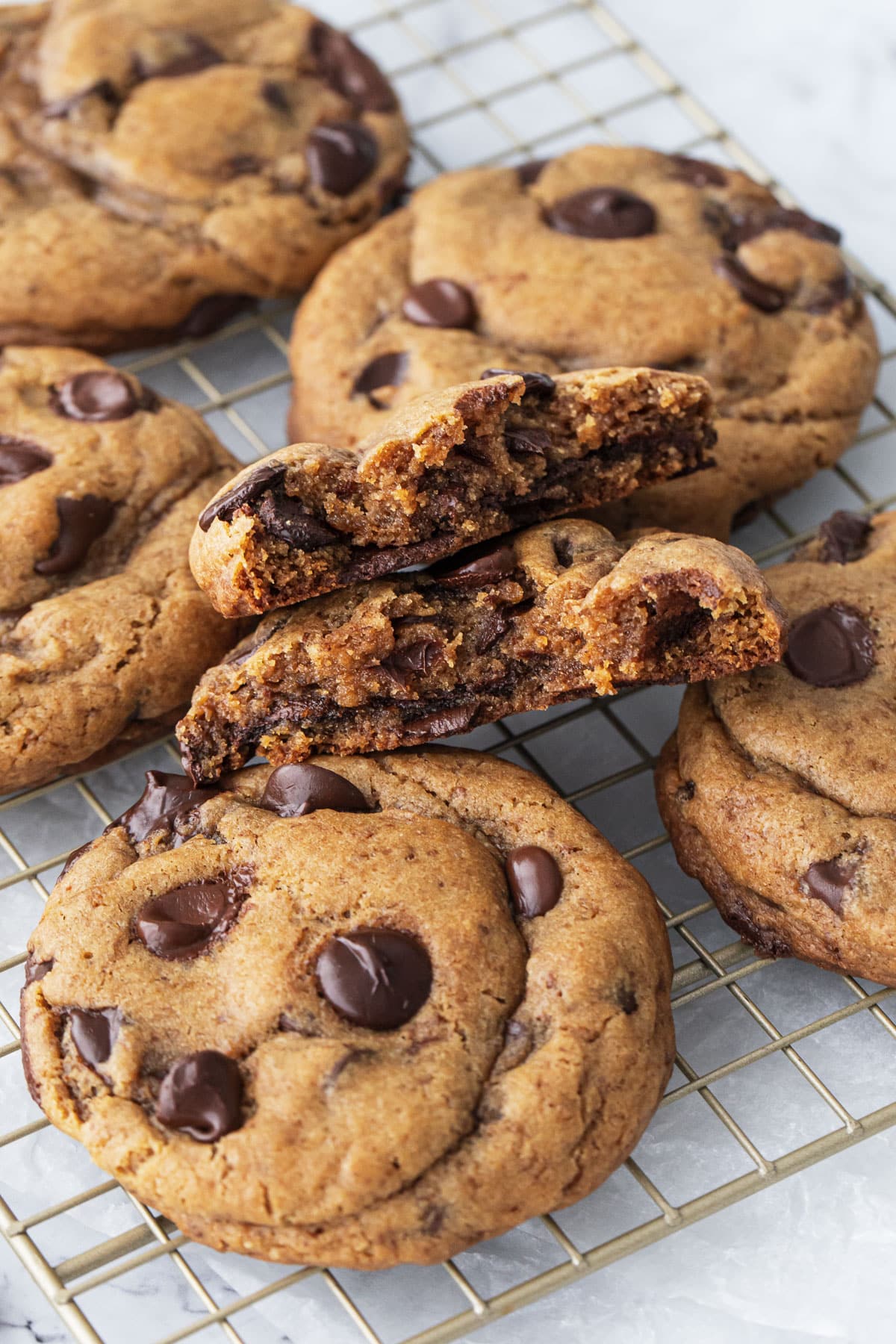 Closeup, jumbo Brown Butter Chocolate Chip Cookies on a wire rack, one broken in half to see the plush, gooey texture inside.