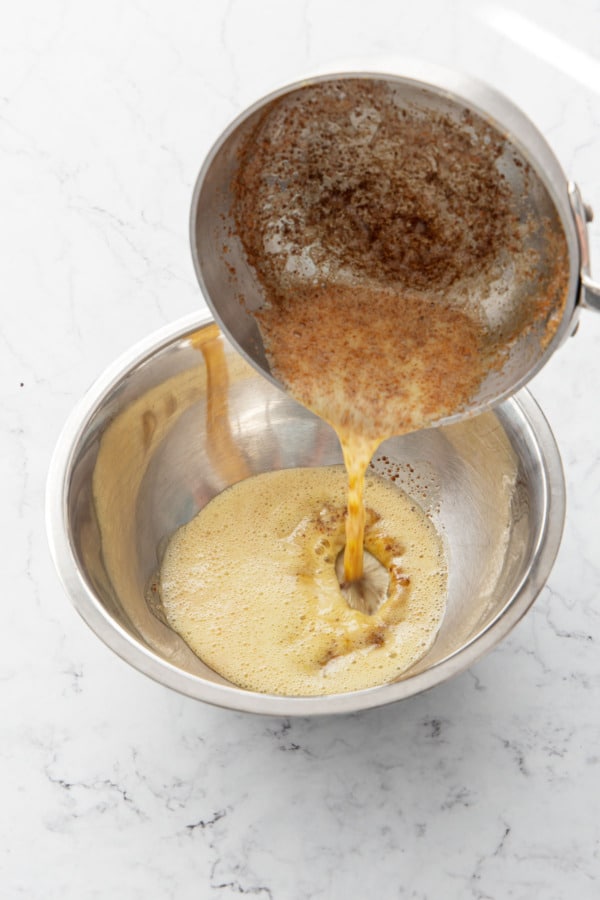 Pouring brown butter into a stainless mixing bowl.