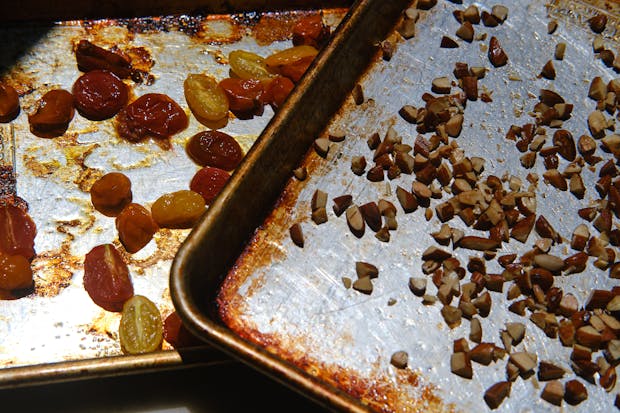 cherry tomatoes roasted on a baking sheet alongside toasted almonds
