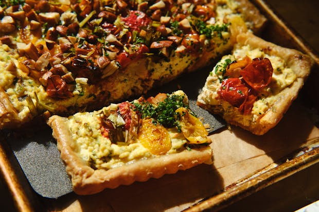 cherry tomato tart with burnt scallion ricotta filling in a tart pan cut into servings