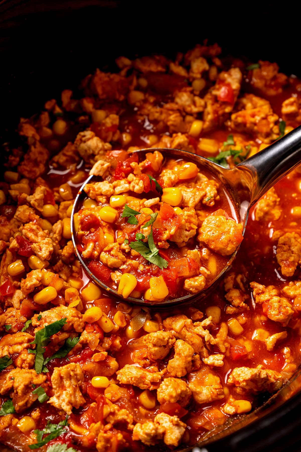 Close up of a ladle scooping turkey chili inside the crock pot.
