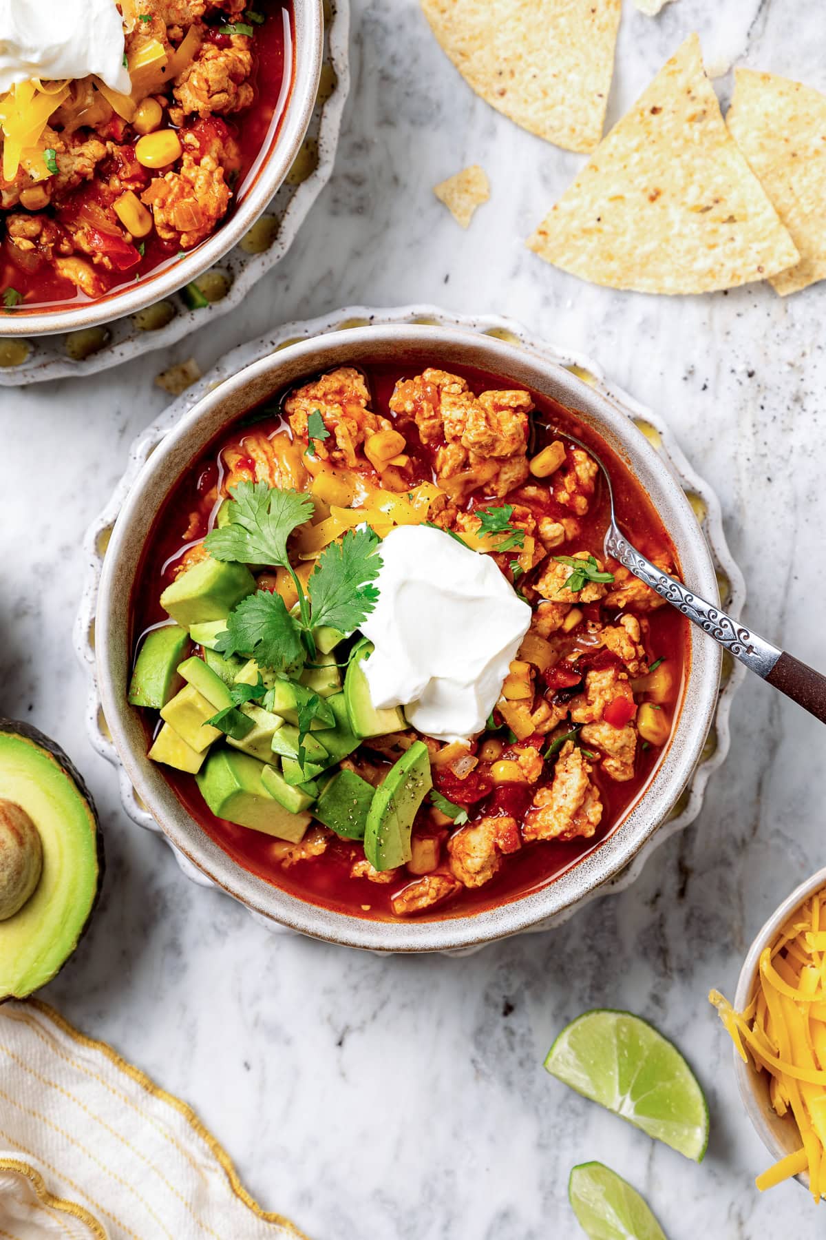 A bowl of turkey chili garnished with sour cream, diced avocado, tortilla chips, and cilantro.